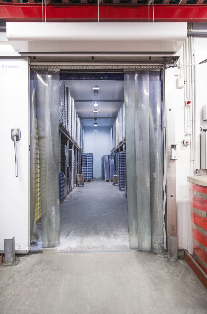 A coolroom featuring industrial shelving units and plastic strip curtains, designed for optimal storage conditions. The environment highlights the importance of coolroom dehumidification to prevent moisture build-up and maintain product quality.